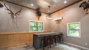 A kitchen with a wooden countertop, bar stools, two windows, and a ceiling with recessed lighting.