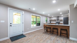 A modern kitchen with a central island, wooden bar stools, and large windows.