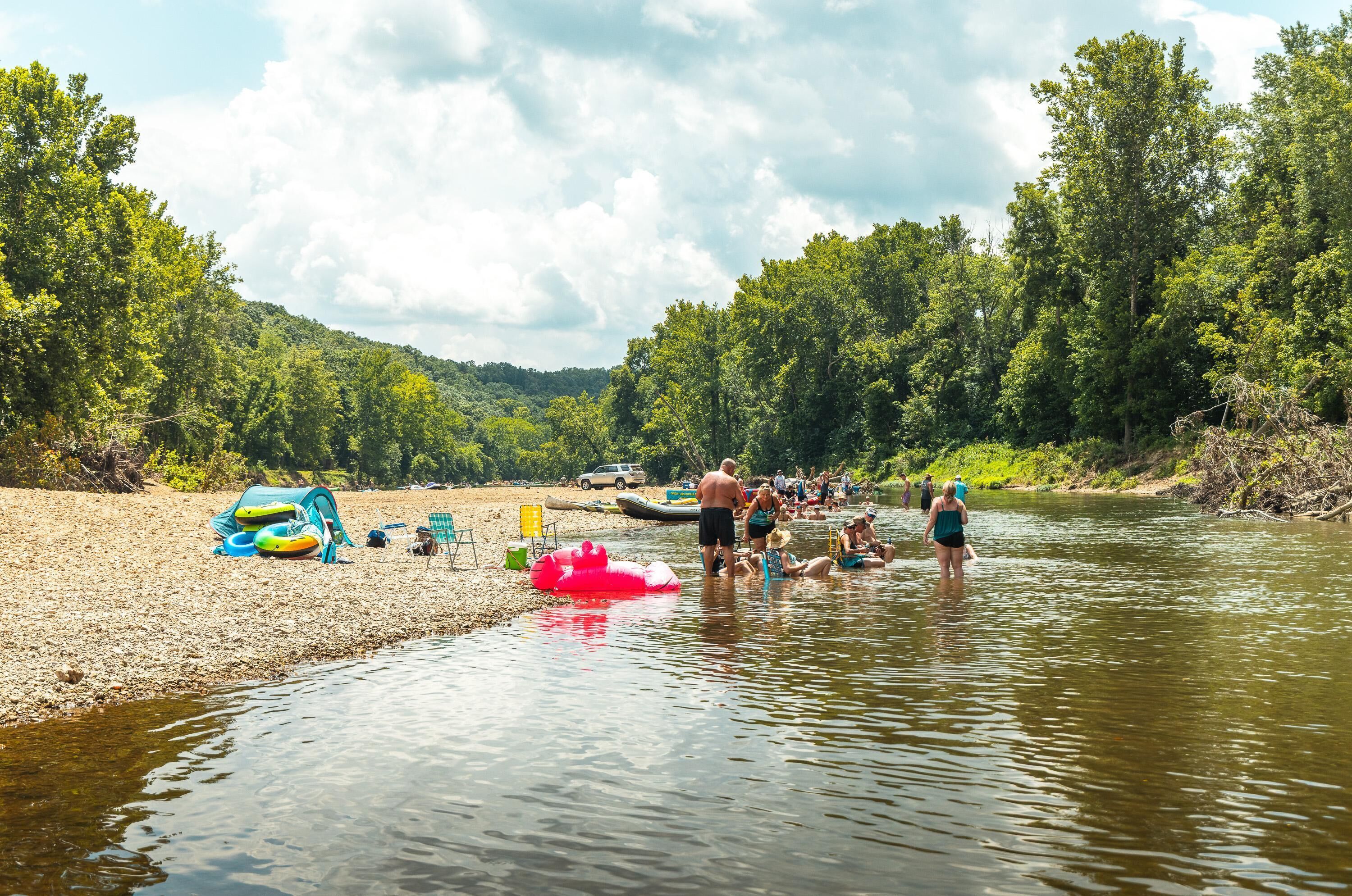 A riverbank with people engaging in water activities, a tent, and a boat.