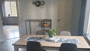 Spiseområde med et træbord, to stole, en potteplante og en dekorativ vægdekoration.