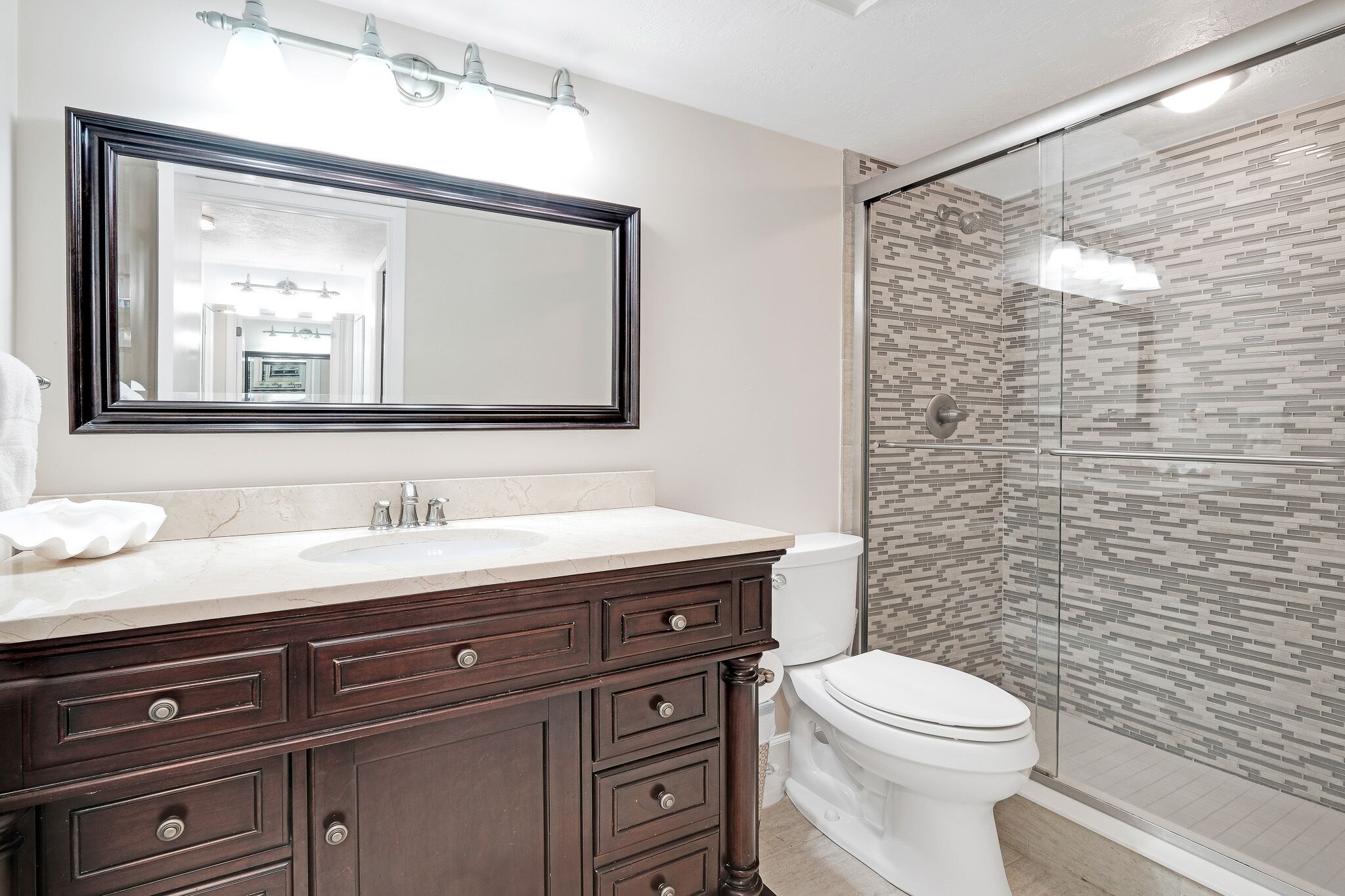 A bathroom with a marble sink, dark wooden vanity, a large mirror, and a glass shower enclosure.