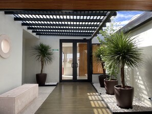 A corridor with a wooden floor, potted plants, and a door marked "SALIDA DE EMERGENCIA".