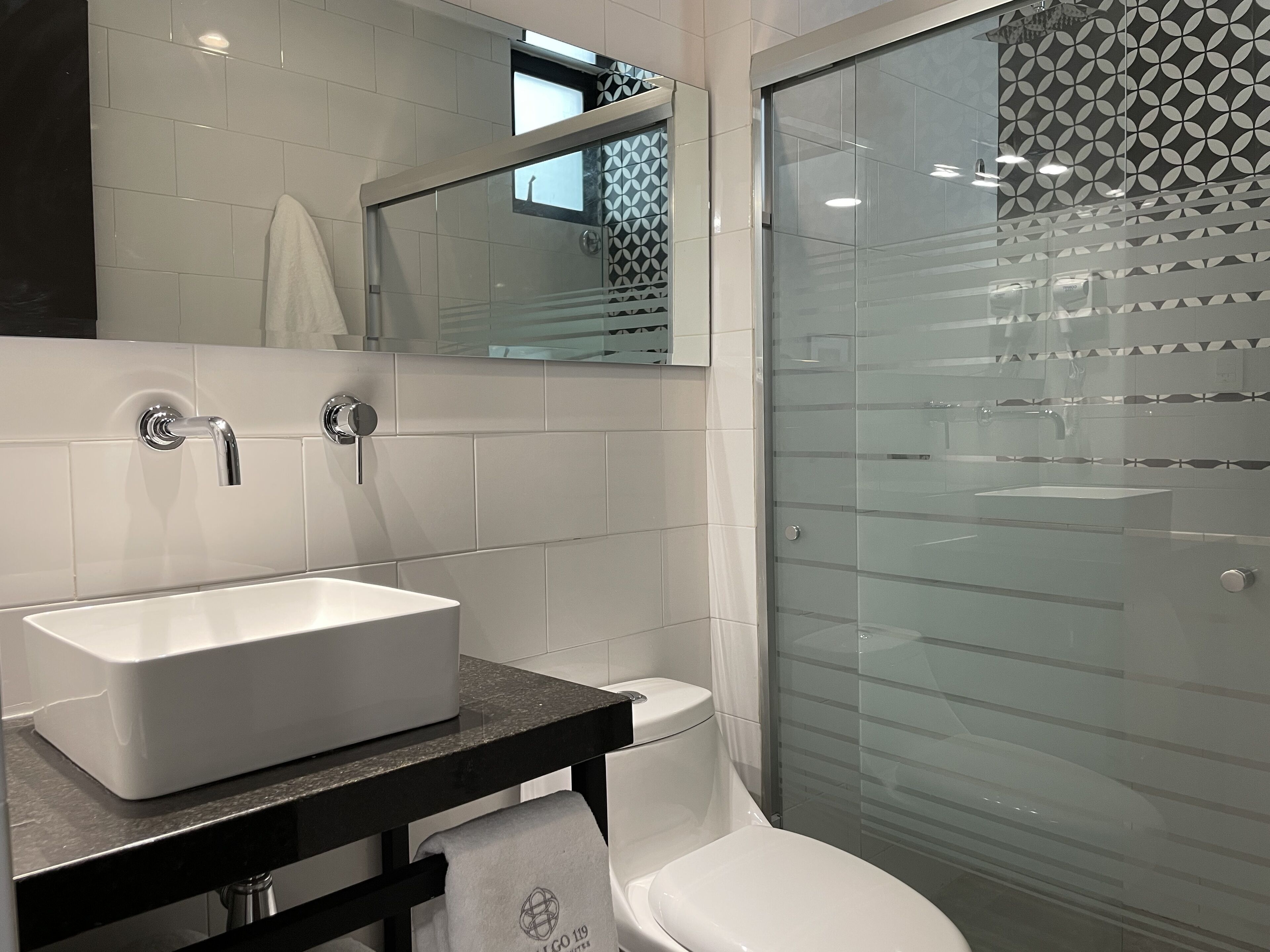 A modern bathroom with a white sink, a toilet, and a glass shower enclosure.