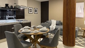 Uma cozinha moderna com armários escuros, bancada de granito e um espaço de refeições com mesa de madeira redonda e cadeiras estofadas cinzas.