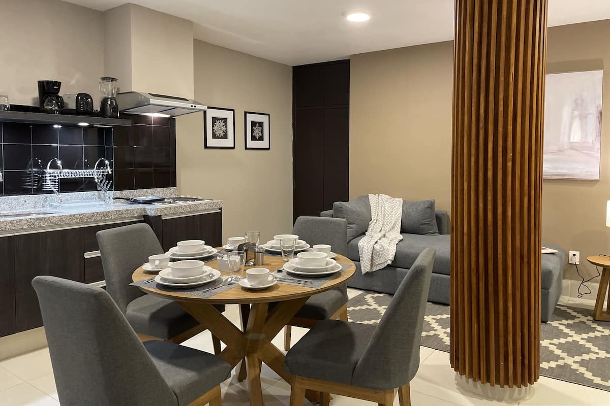 A modern kitchen with dark cabinetry, a granite countertop, and a dining area with a round wooden table and grey upholstered chairs.