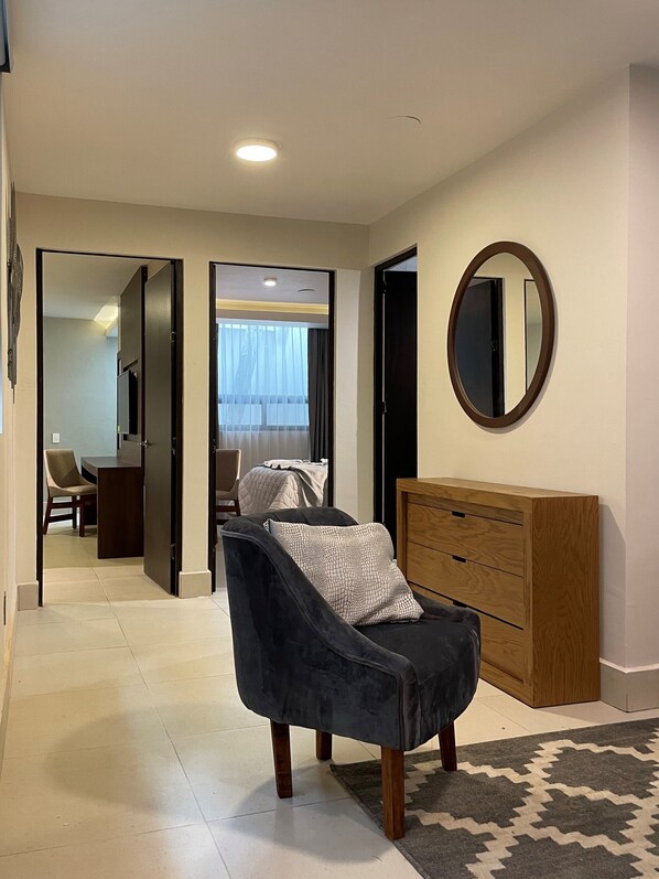 A modern living room with a dark armchair, a wooden dresser, and a mirror on the wall.