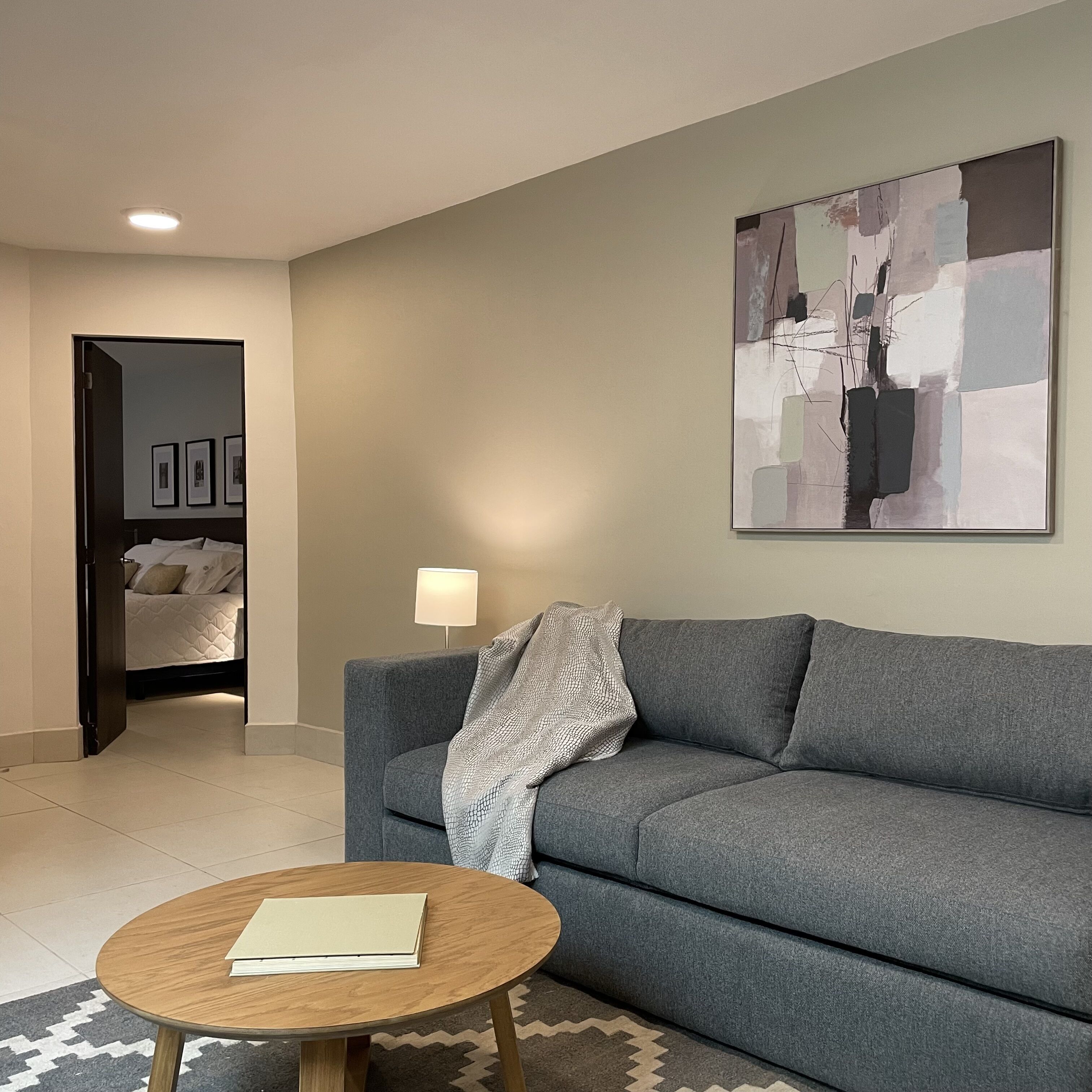 Una sala de estar moderna con un sofá gris, una mesa de centro redonda de madera y un cuadro abstracto grande en la pared.