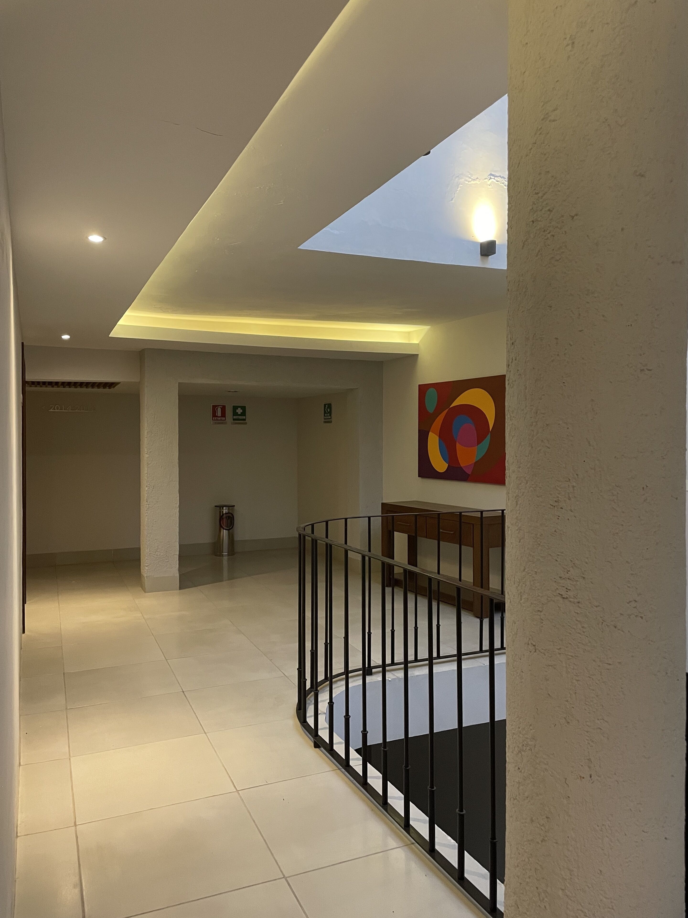 A spacious interior with a skylight, a staircase with a black railing, and a colorful abstract painting on the wall.
