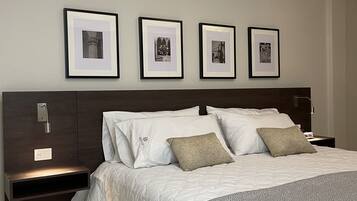 A neatly arranged bedroom with a large bed, a dark wooden headboard, and a nightstand with a lamp. There are four framed pictures on the wall above the bed.