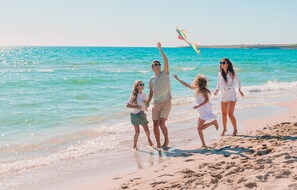 Eine Familie spaziert über einen sandigen Strand, im Hintergrund glares blaues Meer.