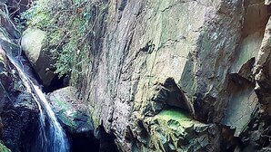 A man standing with arms outstretched in front of a waterfall in a rocky area. - Pousada Sítio Monte Sinai (São José do Barreiro)