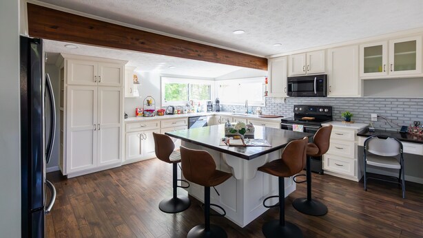 Une cuisine moderne avec des meubles blancs, un îlot central doté de tabourets, un réfrigérateur noir et un four à micro-ondes.