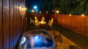 Un bain à remous avec un foyer et des chaises dans une cour arrière, la nuit.