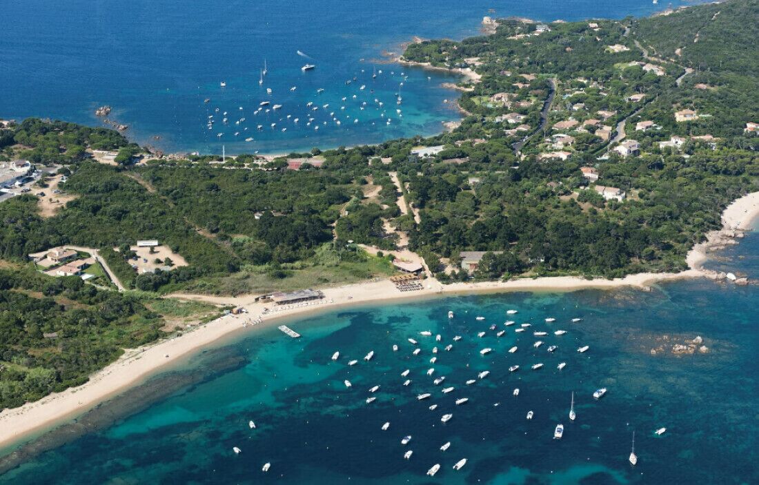 An aerial view of a coastal area with boats, a beach, and scattered buildings.