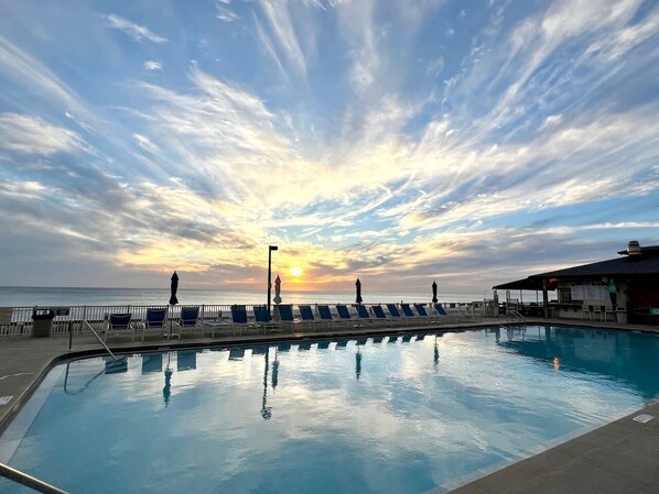 Piscina com cadeiras de descanso e vista para o pôr do sol.