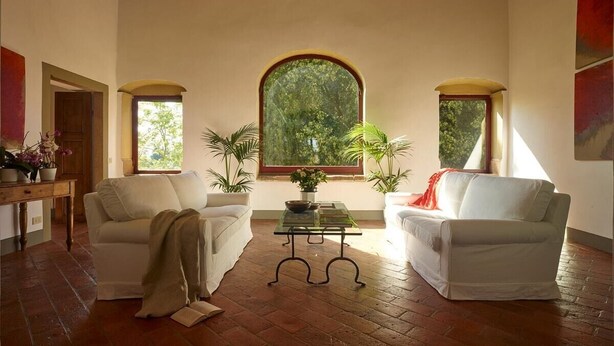 A cozy living room with two white sofas, a glass coffee table, and a large arched window providing a view of greenery. - Villa Stellina - Private Tuscan villa with pool (Tavarnelle Val di Pesa)