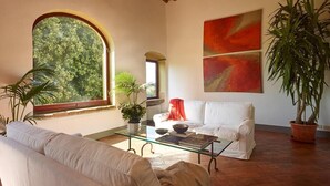 A spacious living room with a large arched window, a white sofa, a glass coffee table, and a potted plant. - Villa Stellina - Private Tuscan villa with pool (Tavarnelle Val di Pesa)