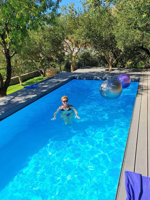 Ein Schwimmbecken mit klarem, blauem Wasser, umgeben von Bäumen und einer Holzterrasse.