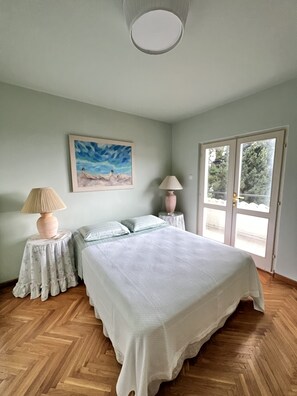 Ein Schlafzimmer mit Bett, zwei Nachttischen, einer Lampe, einem Gemälde und einer Tür mit Blick.