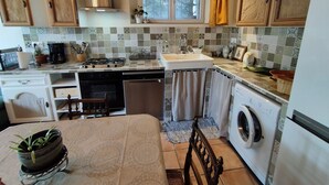 Een keuken met houten kastjes, een fornuis, een spoelbak en een wasmachine.