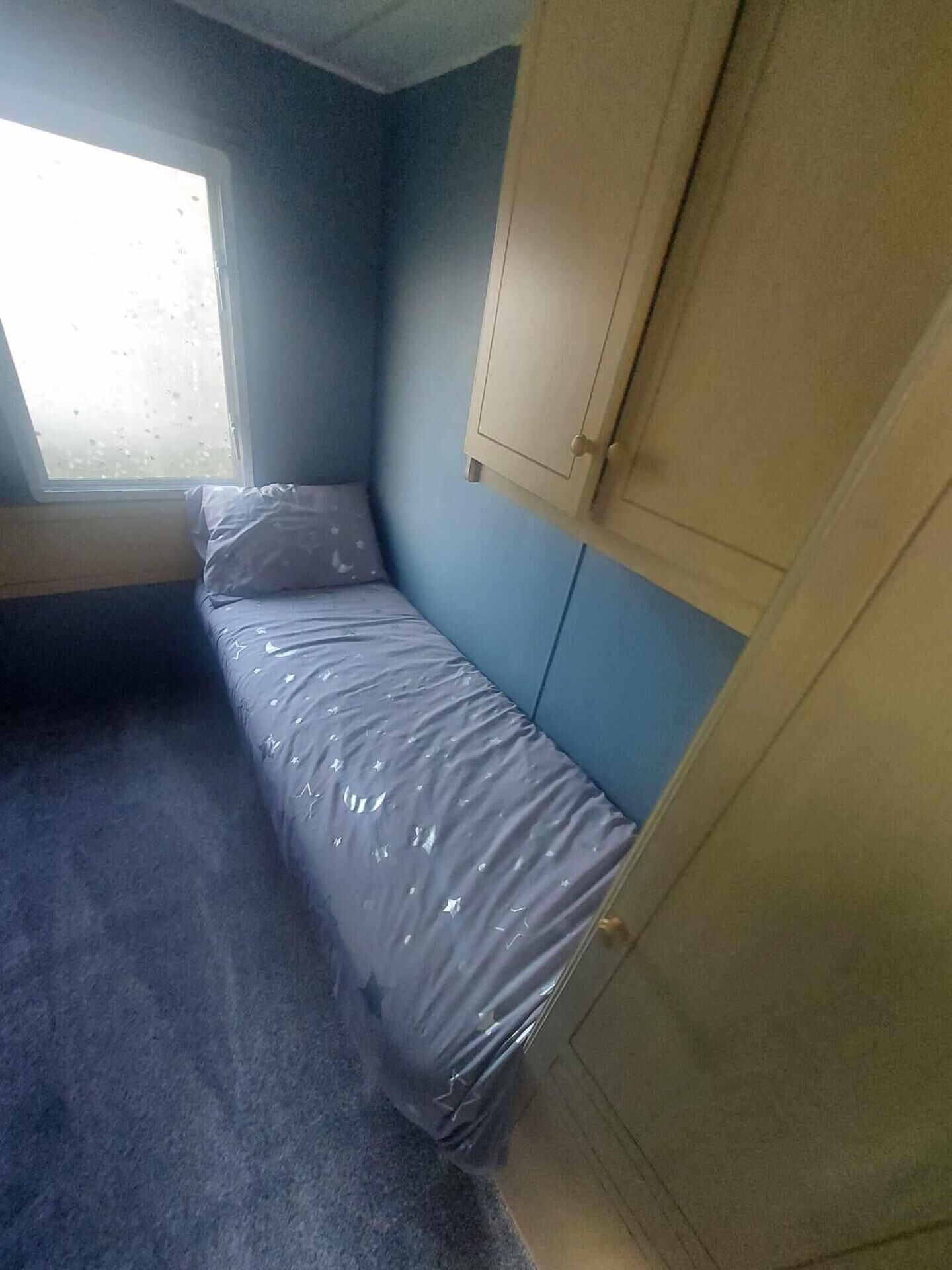A small, single-bed room with a window, a door, and a cabinet.