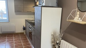 A kitchen with a white refrigerator, a stove, and a sink. There is a window on the left and a radiator on the right.
