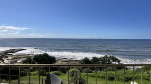 A balcony with a view of the ocean, featuring rocky shoreline and greenery.