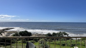 Uitzicht op de kust met een balkon, golven en begroeiing.