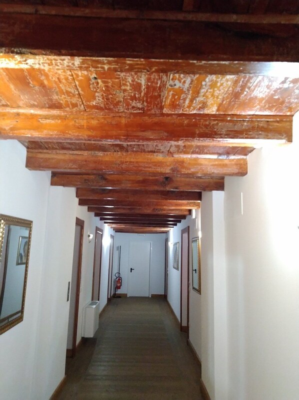 A hallway with wooden beams on the ceiling, white walls, and a carpeted floor. - Grand Hotel Ceresole Reale (Ceresole Reale)