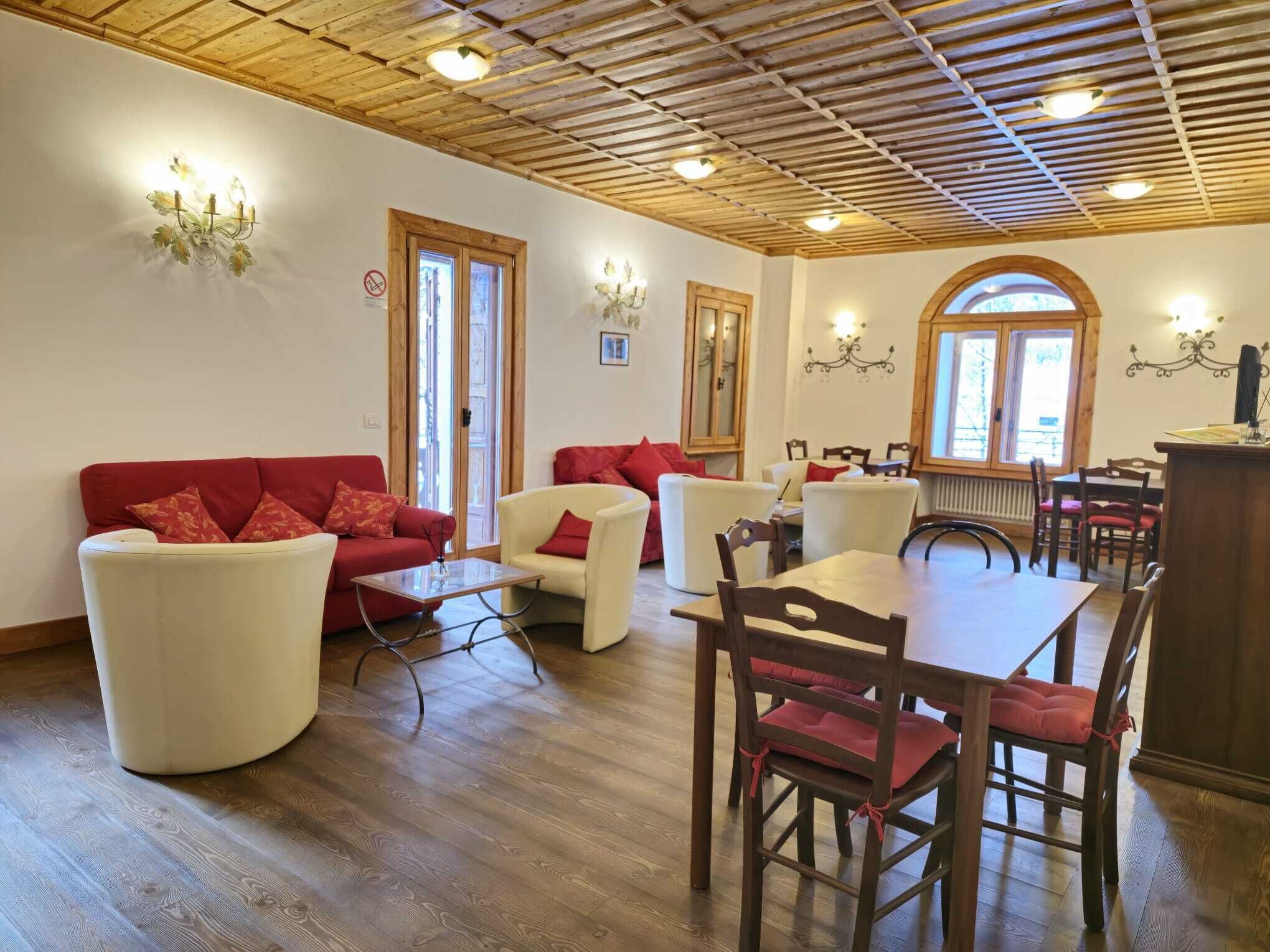 A cozy living room with a wooden ceiling, a dining area with a wooden table and chairs, and a red sofa with matching cushions.