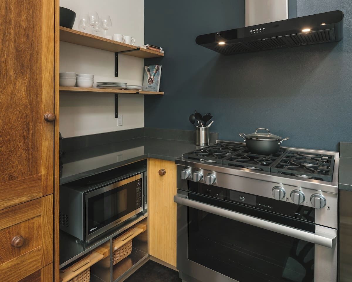 Een keuken met een fornuis, oven, magnetron en houten kastjes.