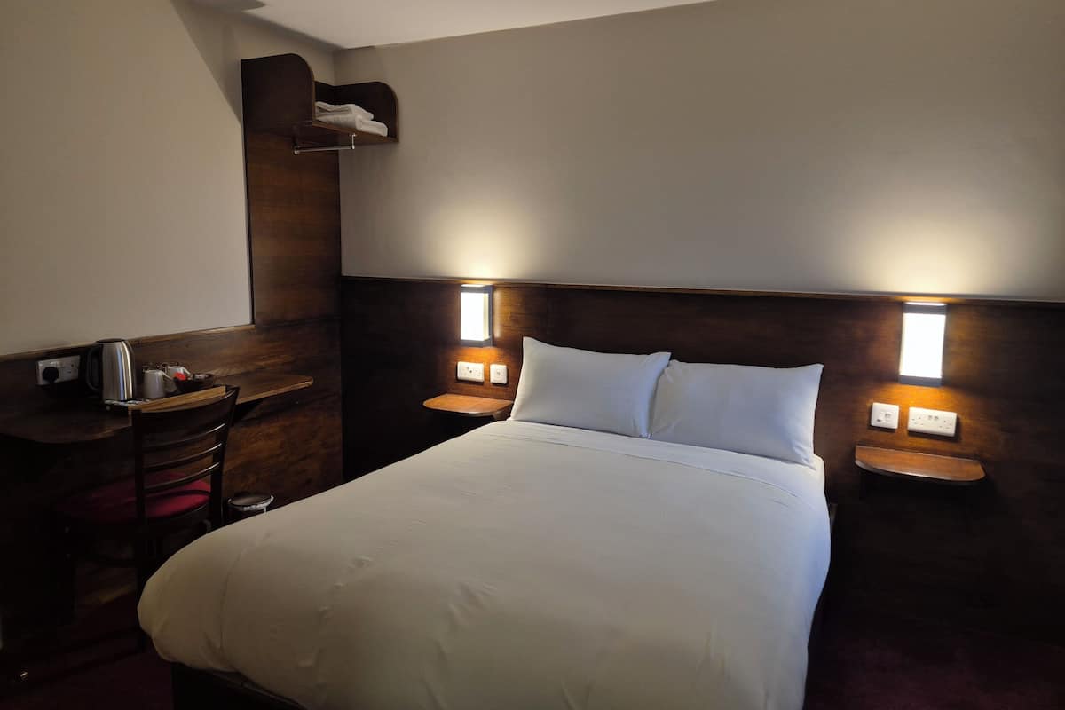 Ein Hotelzimmer mit einem Bett, Nachttischen, einem an der Wand befestigten Regal und einem kleinen Fenster.