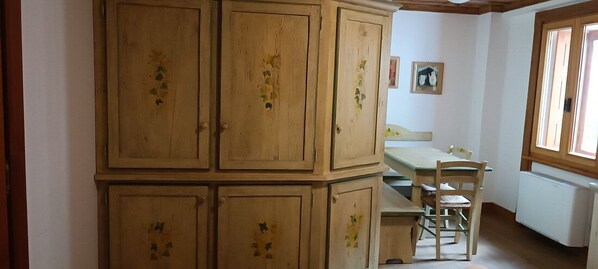 A room with a wooden cabinet with floral designs, a wooden dining table with chairs, and a window with a view. - Residence & Aparthotel Ceresole Reale (Ceresole Reale)