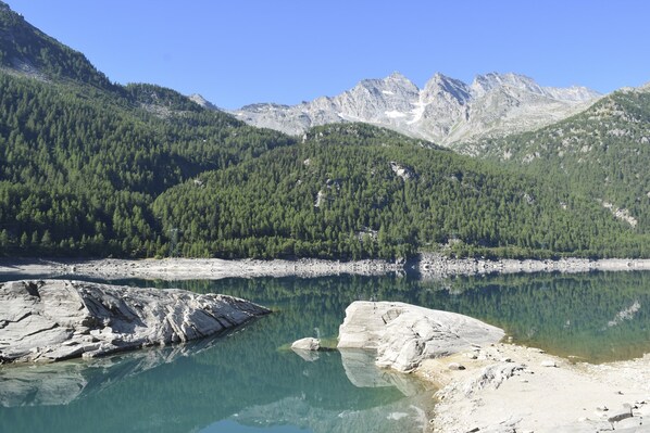 A mountainous landscape with a clear lake, rocky shore, and dense forest.