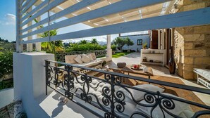 Un espace extérieur aménagé avec un coin salon couvert, comprenant un canapé blanc et une table à manger, le tout entouré d’un mur en pierre et offrant une vue sur le paysage.