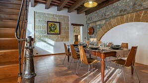 Un espace repas agrémenté d’un mur en pierre, de poutres en bois au plafond et d’un escalier rustique.