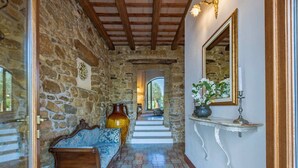 Un couloir aux murs de pierre, avec un banc en bois, un miroir et un vase rempli de fleurs.