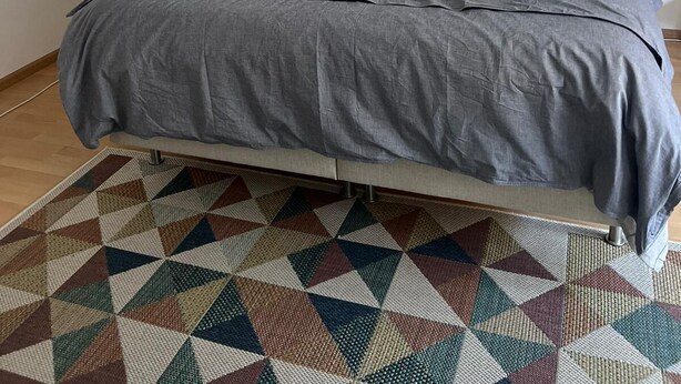 A bedroom with a bed, a nightstand, a lamp, a painting, and a geometric patterned rug. - Gemütliche für die Familien Oder Urlauber (Basel)