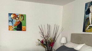 A modern bedroom with a large bed, a bedside table with a lamp, and two paintings on the walls. - Gemütliche für die Familien Oder Urlauber (Basel)