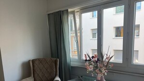 A room with a white table, a brown armchair, and a window with curtains. - Gemütliche für die Familien Oder Urlauber (Basel)