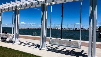 A waterfront walkway with a metal pergola structure, benches, and a view of the marina with boats.