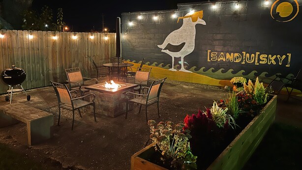 An outdoor patio area with a fire pit, seating, and a mural of a bird on a wall. - Private 3-Bdrm Unit. Historic Home, Downtown Sandusky. Family friendly! (Sandusky)