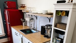 A compact kitchen with a red refrigerator, a coffee maker, and a shelf with dishes and mugs. - Private 3-Bdrm Unit. Historic Home, Downtown Sandusky. Family friendly! (Sandusky)