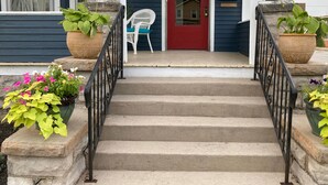 A front entrance with a red door, a white chair, and potted plants on either side of the steps. - Private 3-Bdrm Unit. Historic Home, Downtown Sandusky. Family friendly! (Sandusky)