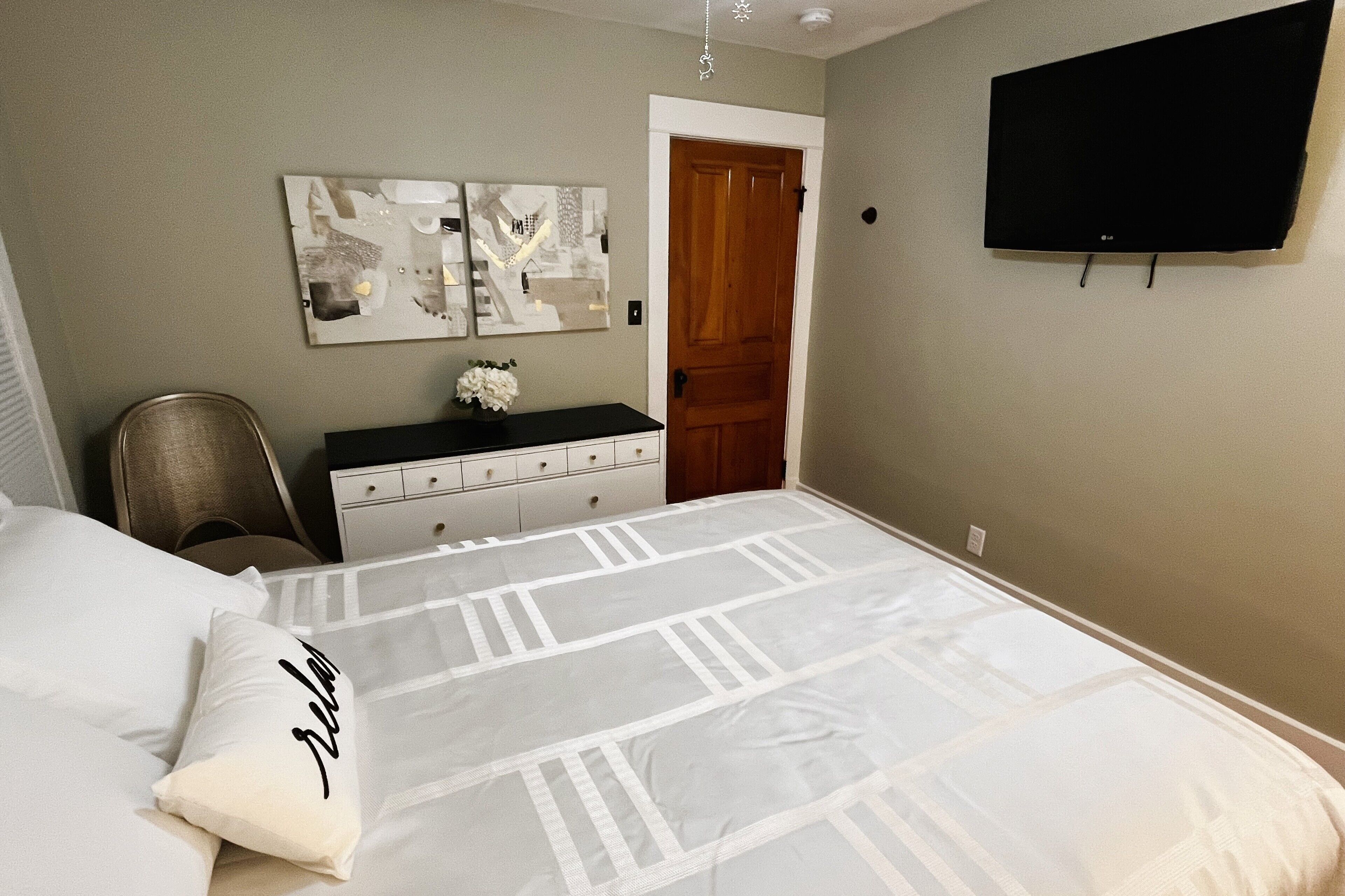 Een slaapkamer met een bed, een kaptafel, een stoel en een aan de muur bevestigde televisie.