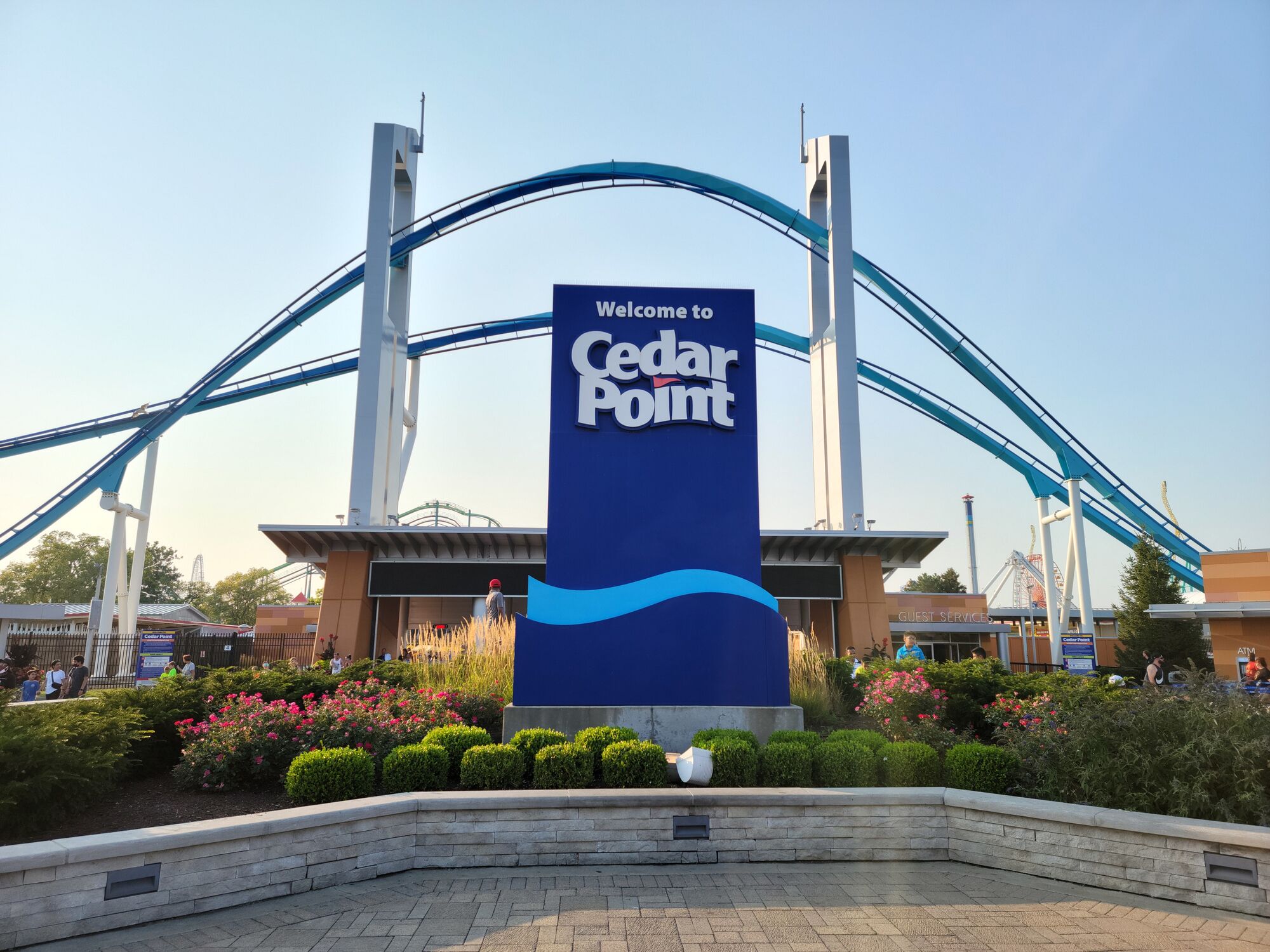 A Cedar Point amusement park entrance with a large sign, roller coaster tracks, and landscaped gardens.