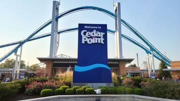 A Cedar Point amusement park entrance with a large sign, roller coaster tracks, and landscaped gardens.