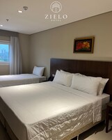 Habitación de hotel con una cama grande, una cama más pequeña, una mesita de noche, un teléfono y un cuadro en la pared.