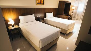 A hotel room with two beds, a bedside table with a lamp, a telephone, a wardrobe, and a painting on the wall.