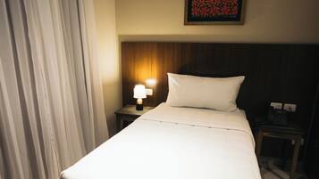 Habitación de hotel con una cama grande, una mesita de noche con lámpara, un cuadro en la pared y una ventana con cortinas.